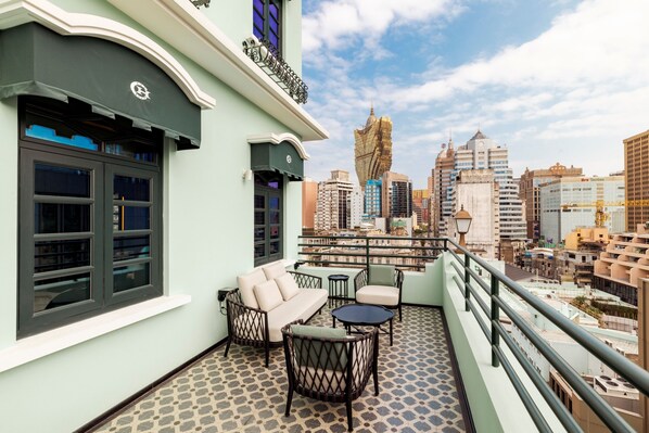 Un balcon aménagé avec un canapé, des chaises et une petite table, offrant une vue sur le paysage urbain et ses différents bâtiments.