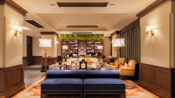 A hotel lobby with a checkered floor, a blue sofa, a bookshelf, and two lamps. - Hotel Central (Macau)