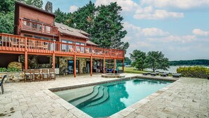 A two-story house with a swimming pool, outdoor seating, and a view of a lake.