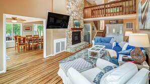 A spacious living area with a stone fireplace, a dining area with wooden furniture, and a balcony with a wooden railing.
