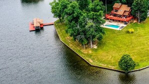 An aerial view of a lakeside property with a large house, a dock, and a swimming pool.