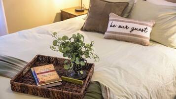 Een netjes opgemaakt bed met een sierkussen waarop staat 'wees onze gast', een kleine plant en een dienblad met een boek en een kaars.