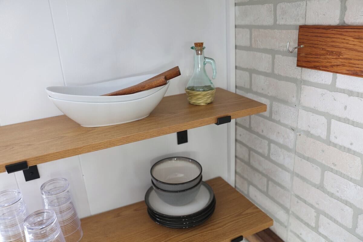 A kitchen shelf with a white bowl, a glass bottle, and stacked plates.