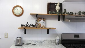 Una cuina amb taulell de marbre, torradora, rellotge, cartell de benvinguda, un ocell decoratiu i una campana extractora d'acer inoxidable.