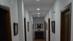 Un couloir aux murs blancs, avec des portes en bois et des tableaux encadrés accrochés aux murs.