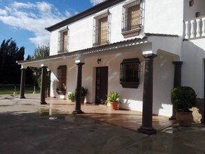 Un edificio de dos pisos con un patio cubierto, columnas y plantas en macetas.