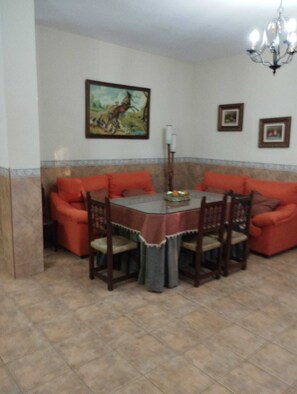 Un comedor con una mesa redonda, cuatro sillas y dos sofás rojos. Hay una araña en el techo sobre la mesa y un cuadro en la pared.