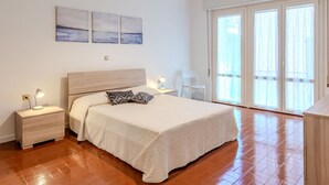 Un dormitorio con cama de madera, mesitas de noche, una lámpara colgante y vistas al exterior a través de un ventanal grande.