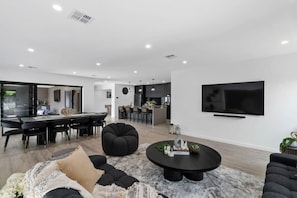 A modern living room with a dining area, kitchen, and a TV mounted on the wall.