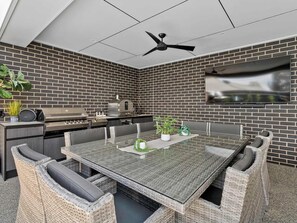 Une cuisine extérieure moderne avec un mur en briques, un ventilateur de plafond et un téléviseur à écran plat fixé au mur.