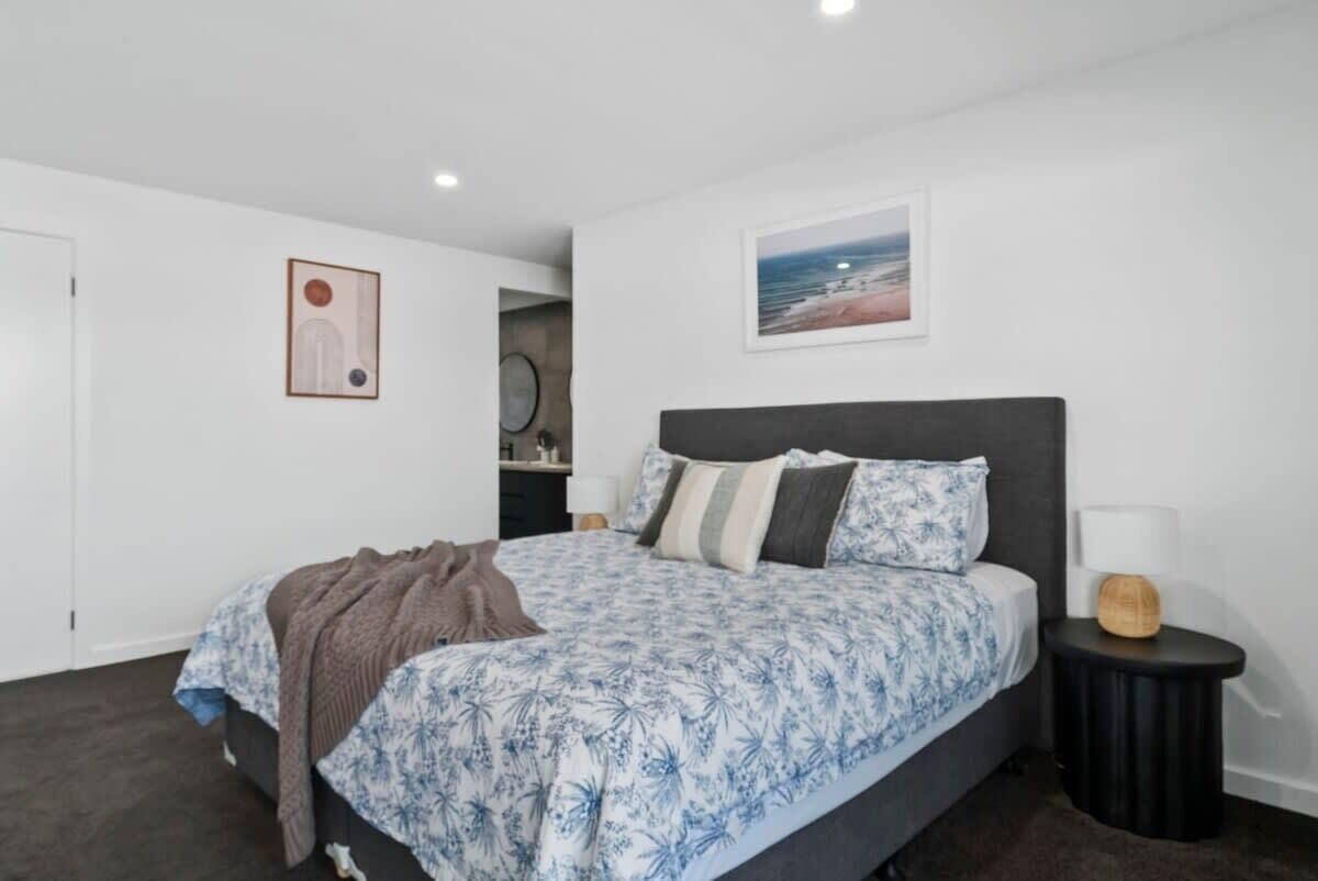 A bedroom with a bed, a nightstand, a wall-mounted picture, and a door.