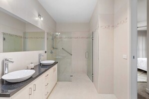 Ein modernes Badezimmer mit einer Duschkabine, einem großen Spiegel und einem Doppelwaschtisch.