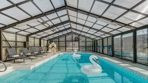 Une piscine intérieure avec des parois en verre transparent, des chaises longues et des bouées en forme de cygne.