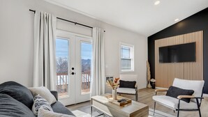 Un salon moderne comprenant un canapé, une table basse, un fauteuil et un téléviseur fixé au mur.