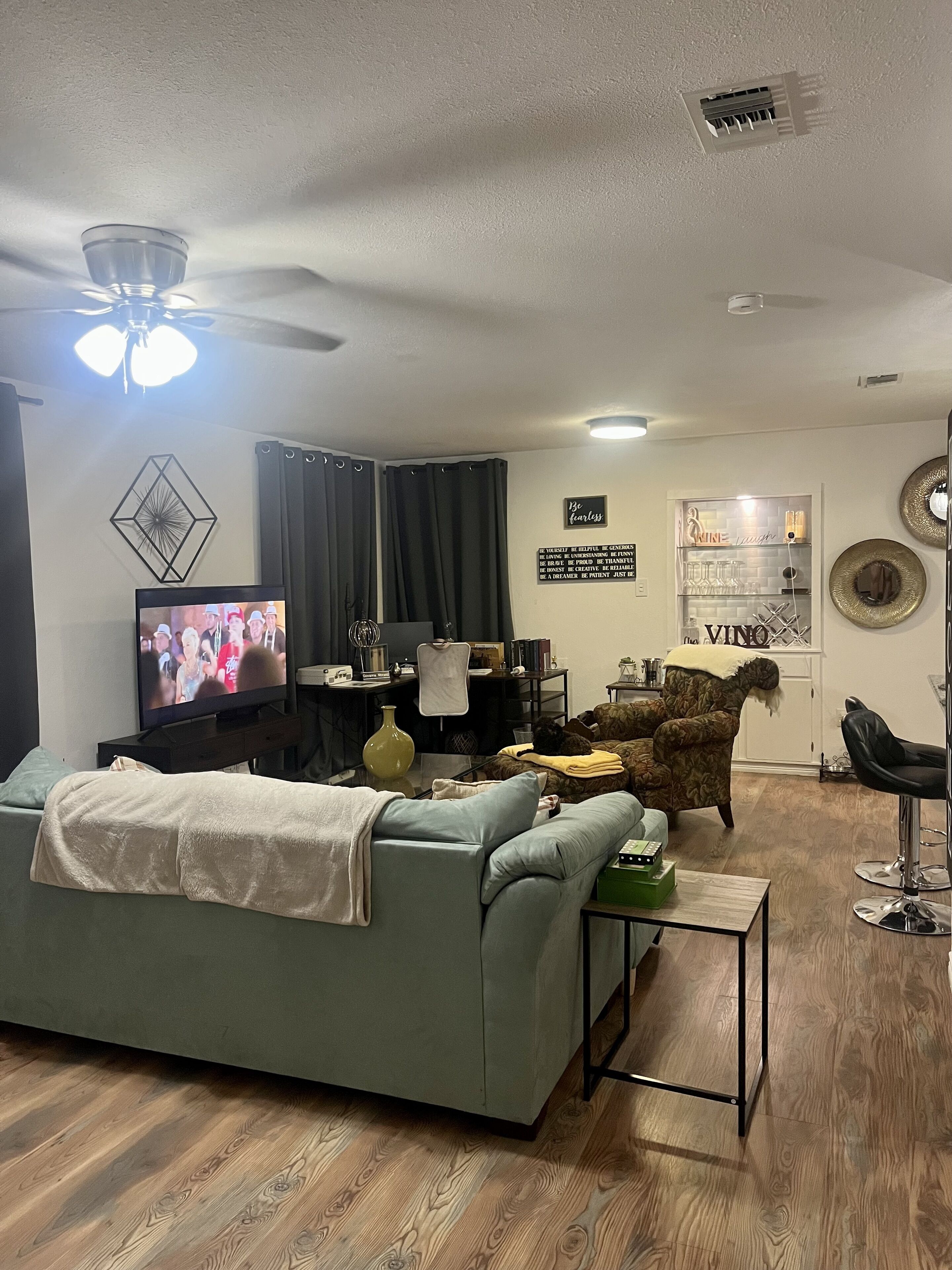 A living room with a sofa, a coffee table, a TV, a ceiling fan, and a cabinet with decorative items.
