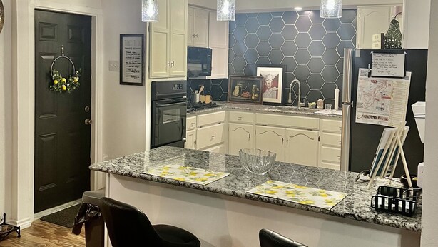 A modern kitchen with a granite countertop, white cabinets, a black backsplash, and three pendant lights. - Charming, cozy 3-bedroom country home in beautiful Seguin, TX (Seguin)