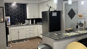 A modern kitchen with white cabinets, a black refrigerator, and a granite countertop. There are pendant lights and a black trash bin. - Charming, cozy 3-bedroom country home in beautiful Seguin, TX (Seguin)
