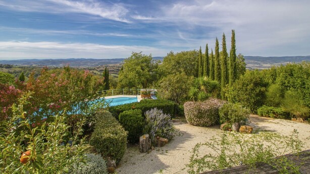 Un jardín ajardinado con piscina, arbustos variados y altos cipreses.