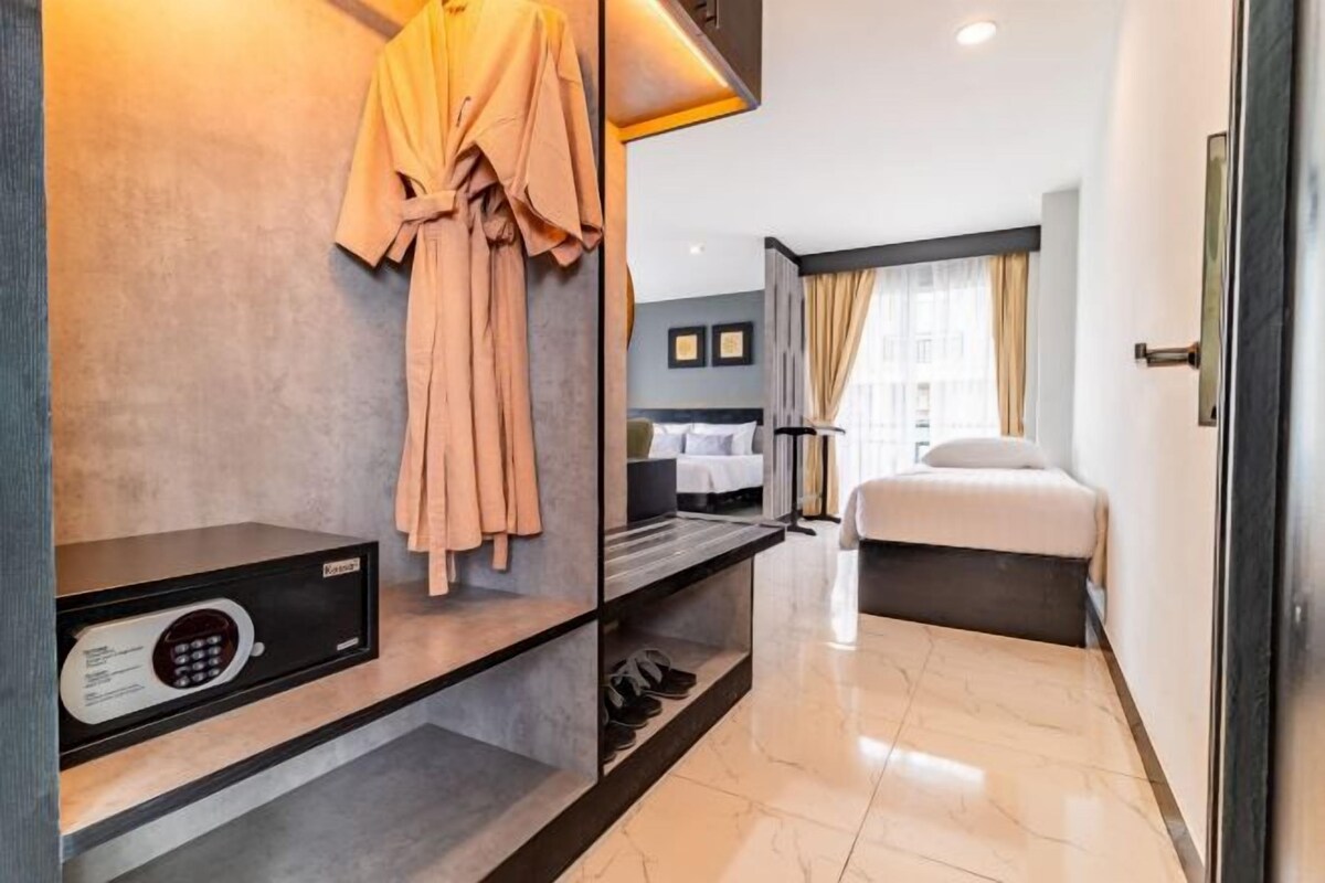 A hotel room with a bed, a bedside table with a radio, and a robe hanging on the wall.