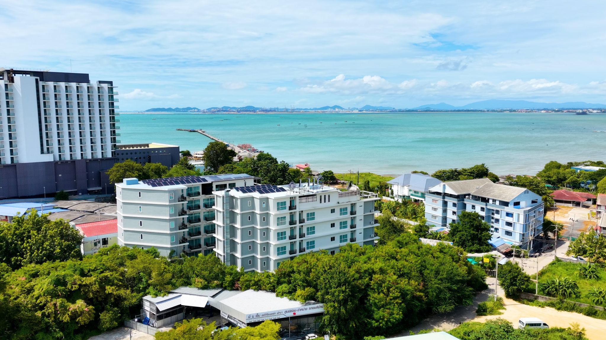 A coastal hotel with multiple buildings, including a high-rise and several mid-rise structures, surrounded by lush greenery and a view of the sea.