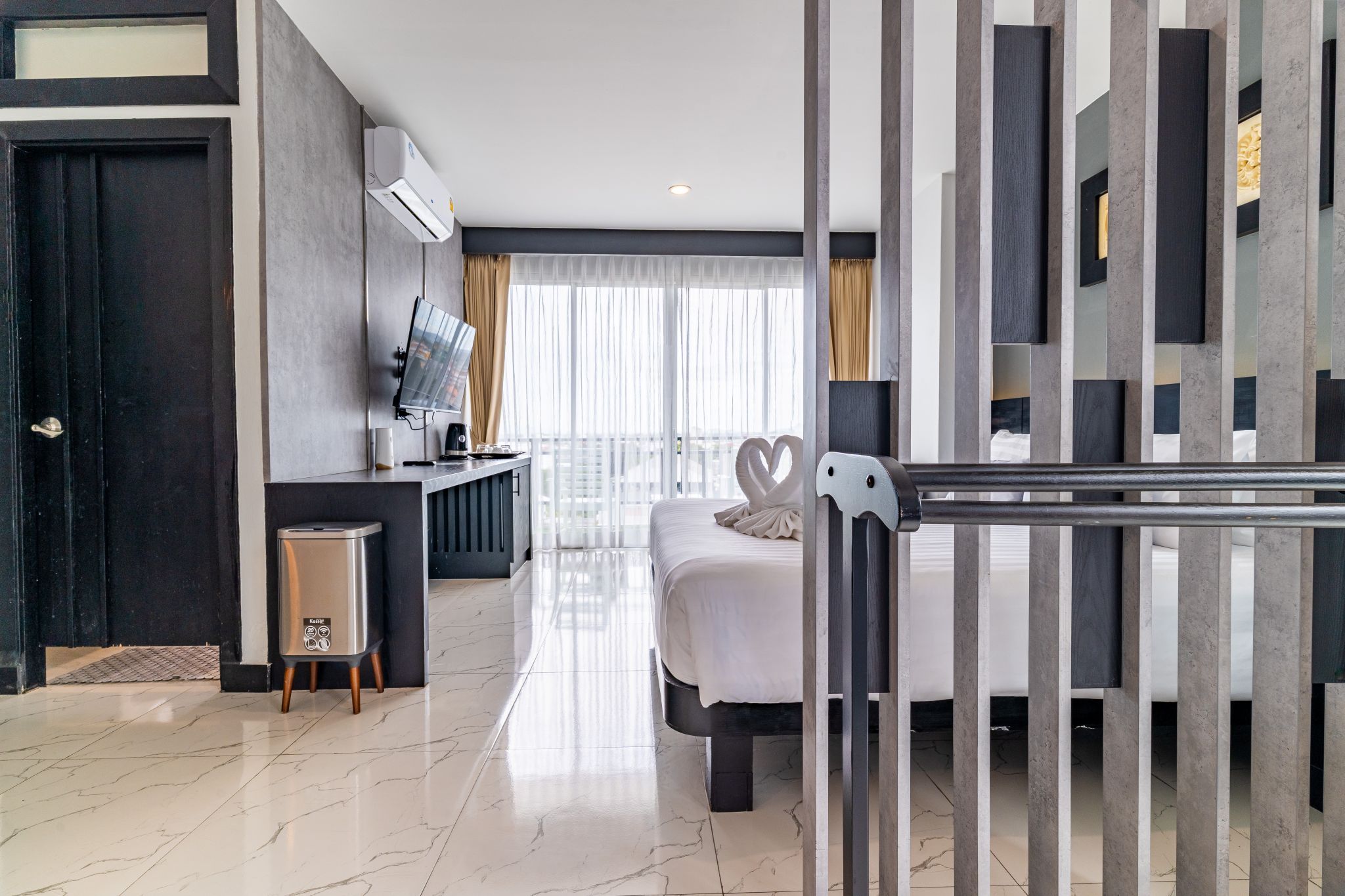 A modern hotel room with a bed, a desk, a television, and a minibar.