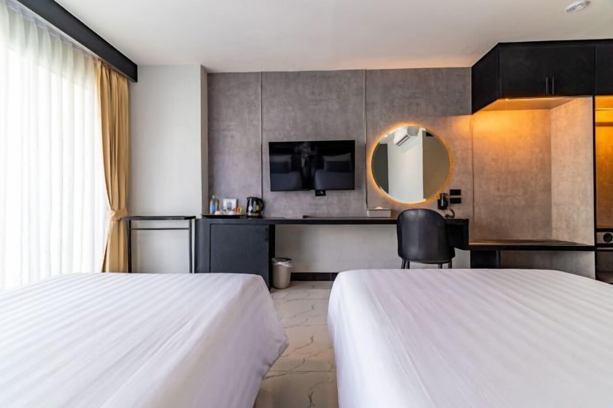 A hotel room with two beds, a desk, a TV, and a mirror.