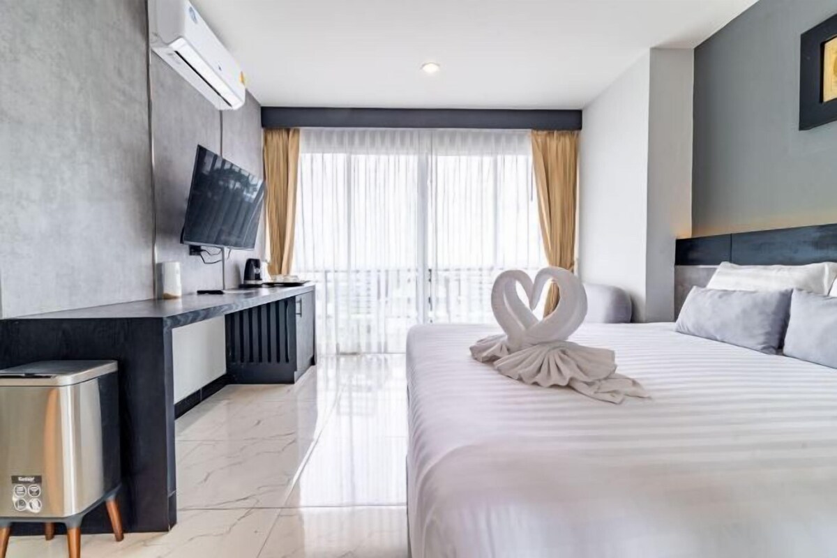 A hotel room with a bed, a desk, a television, and a view of the outdoors.