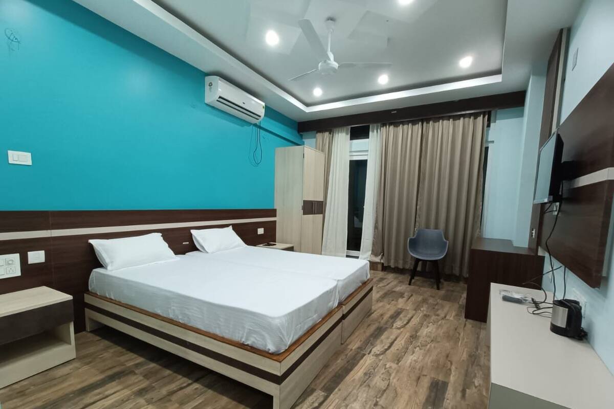 Una habitación de hotel moderna con piso de madera, una cama con ropa blanca, un escritorio con silla y un televisor montado en la pared.