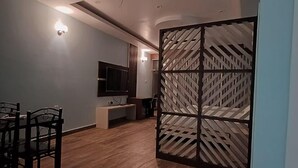 A modern living room with a ceiling fan, a dining area with chairs, a TV, and a decorative partition. - River King City Palace (Guwahati)