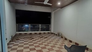 A spacious indoor area with a checkered floor, a ceiling fan, and a view through a large window to the outside. - River King City Palace (Guwahati)