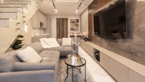 Ein modernes Wohnzimmer mit einem grauen Sofa, einem runden Couchtisch und einem großen Flachbildfernseher an der Wand.