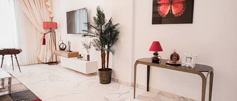 A modern living room with a marble floor, a white console table, a red lamp, a potted plant, and a wall-mounted TV.