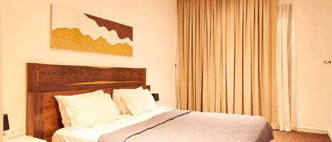 A neatly made bed with a wooden headboard, a bedside table, and a large window with curtains.