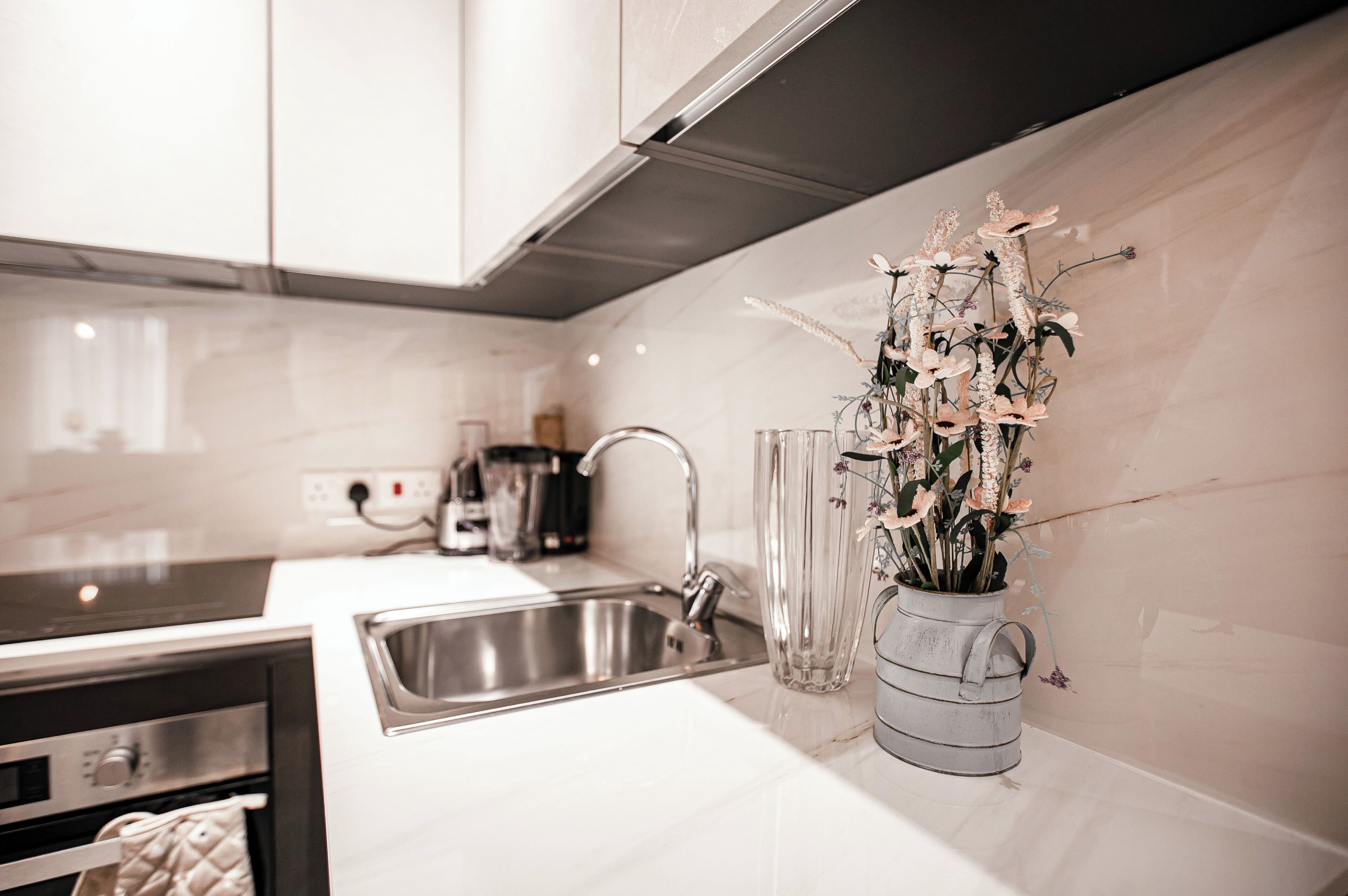 Une cuisine moderne équipée d’appareils électroménagers en acier inoxydable, d’un évier et d’un vase rempli de fleurs posé sur le plan de travail.