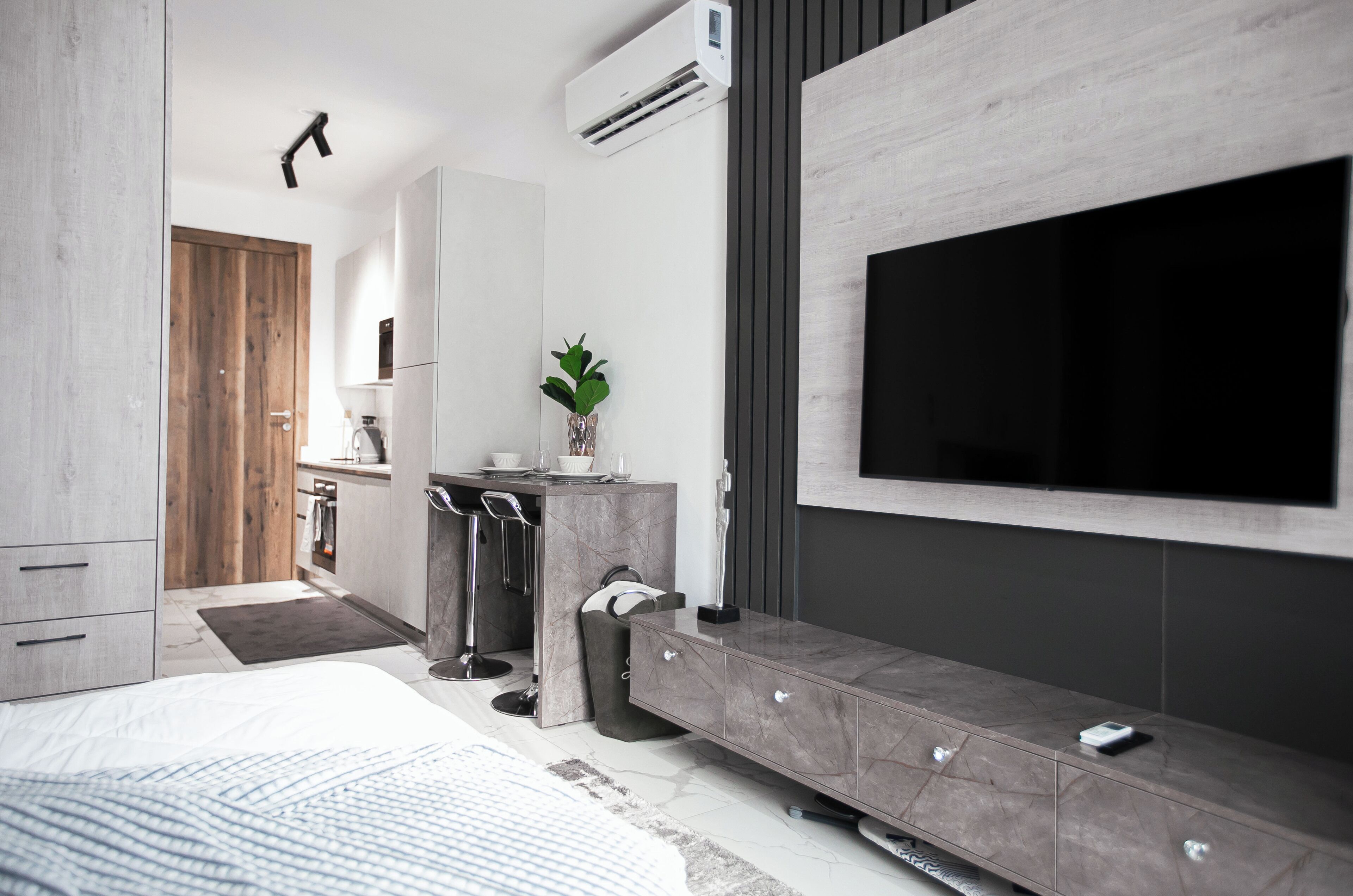 Une chambre à coucher moderne avec un lit, un téléviseur fixé au mur, une table de chevet et une armoire intégrée.