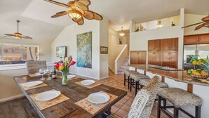 A modern kitchen with wooden cabinets, a central island, and a dining area with a large table and bar stools.