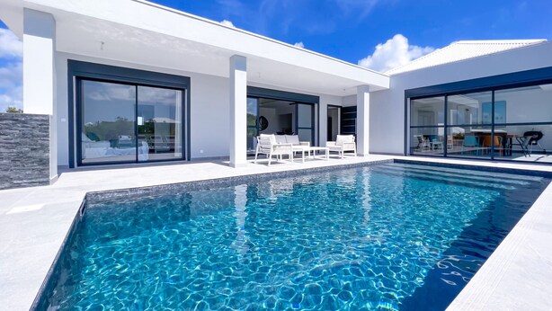 Una casa moderna con piscina, puertas de cristal amplias y mobiliario de exterior.