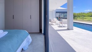 Un dormitorio moderno con una cama grande, un armario y vistas a un patio exterior con piscina y zona de estar.