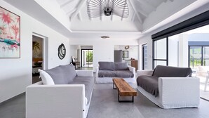 Amplia sala de estar con muebles modernos, ventilador de techo y ventanas grandes que ofrecen vistas al exterior.