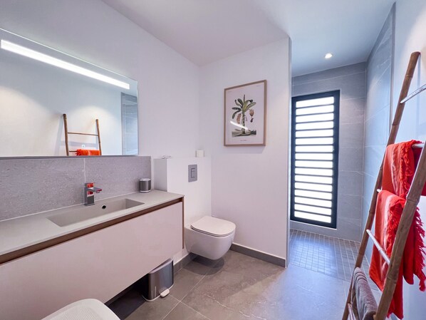 A modern bathroom with a large mirror, a sink, a toilet, and a shower area.