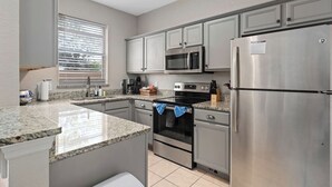 Una cocina moderna con encimeras de granito, electrodomésticos de acero inoxidable y una ventana con persianas.