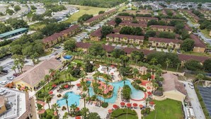 Vista aérea de un complejo turístico con una piscina central, varias edificaciones y follaje circundante.