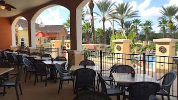 An outdoor dining area with tables and chairs, a pool, and palm trees.
