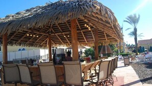 A thatched-roof outdoor bar area with wicker chairs and a wooden counter. - Mario Kart Mayhem at Regal Palms Resort | Sage Vacations (Davenport)