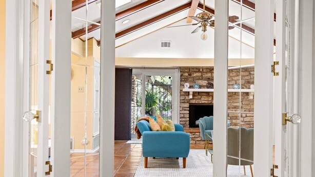 Amplio salón con chimenea de piedra, dos sillones azules y un ventanal con vistas a un jardín.