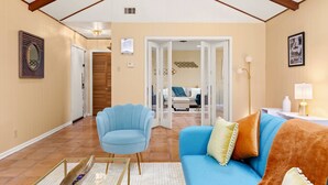 Amplia sala de estar con techo alto, un sillón azul, un sofá azul con cojines y una puerta de madera al fondo.