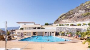 Et moderne hotel med swimmingpool, udendørs siddepladser og udsigt til bjergene.