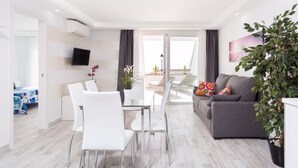 En moderne stue med en grå sofa, hvide stole, et spisebord og en stor potteplante.