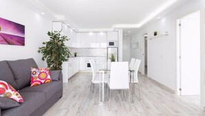 En moderne lejlighed med en grå sofa, et spisebord med stole, et køkken og en opholdsstue.