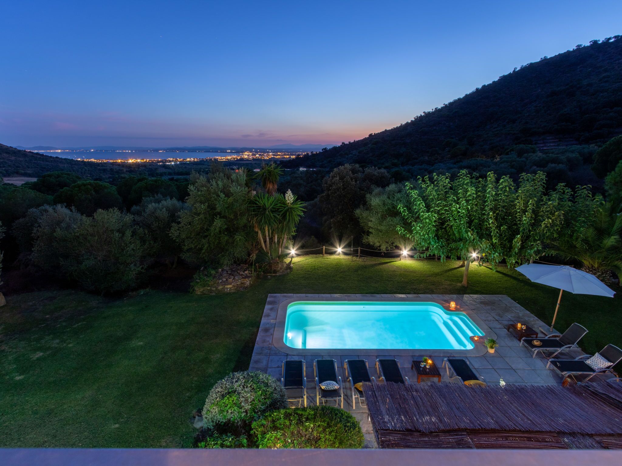 A rectangular pool with a clear blue water surface, surrounded by a well-maintained lawn and a variety of trees.